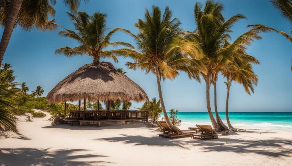 A serene beach with crystal-clear waters and a clear blue sky, with the sun shining and palm trees swaying in the soft breeze. The sand is warm and golden, inviting you to take a dip in the refreshing ocean water or relax under the shade of an umbrella. The perfect temperature for a day at the beach in Tulum, Mexico.